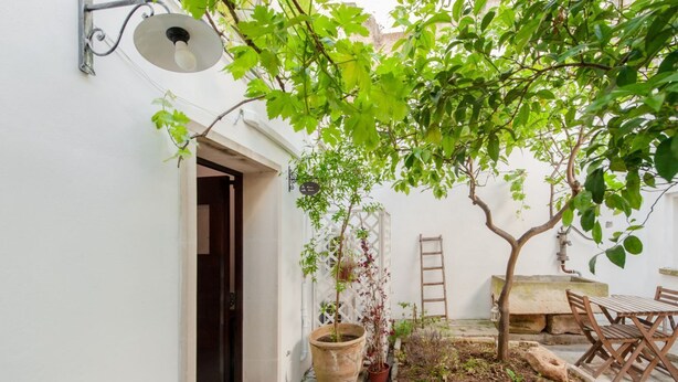 A courtyard with a door, potted plants, a wooden table, and a chair. - GuestHost - Palazzo Rolli La Stanza della Libreria (Galatone)