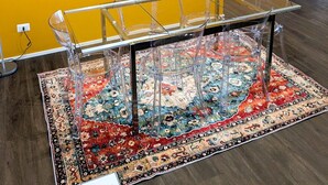Un comedor con una mesa y sillas de vidrio, un tapete estampado y obras de arte en las paredes.
