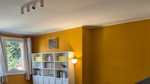 Una sala de estar con sofá, lámpara, estantería y ventana con cortinas.