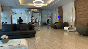 A modern lobby with a curved sofa, a glass coffee table, and a reception area with a digital screen. - Green Residences Taft Ave. by darpm (Manila)