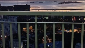A balcony with a view of a cityscape at dusk, featuring buildings and a body of water with boats. - Green Residences Taft Ave. by darpm (Manila)