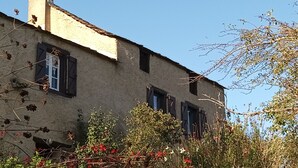 A rustic building with a chimney, multiple windows with shutters, and a garden with red flowers in front. - Vacation rental in the middle of the Viaur Gorges (Pampelonne)