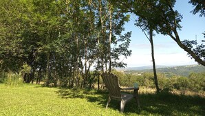 A grassy area with a single wooden chair and a table, surrounded by trees and a distant view of a valley. - Vacation rental in the middle of the Viaur Gorges (Pampelonne)