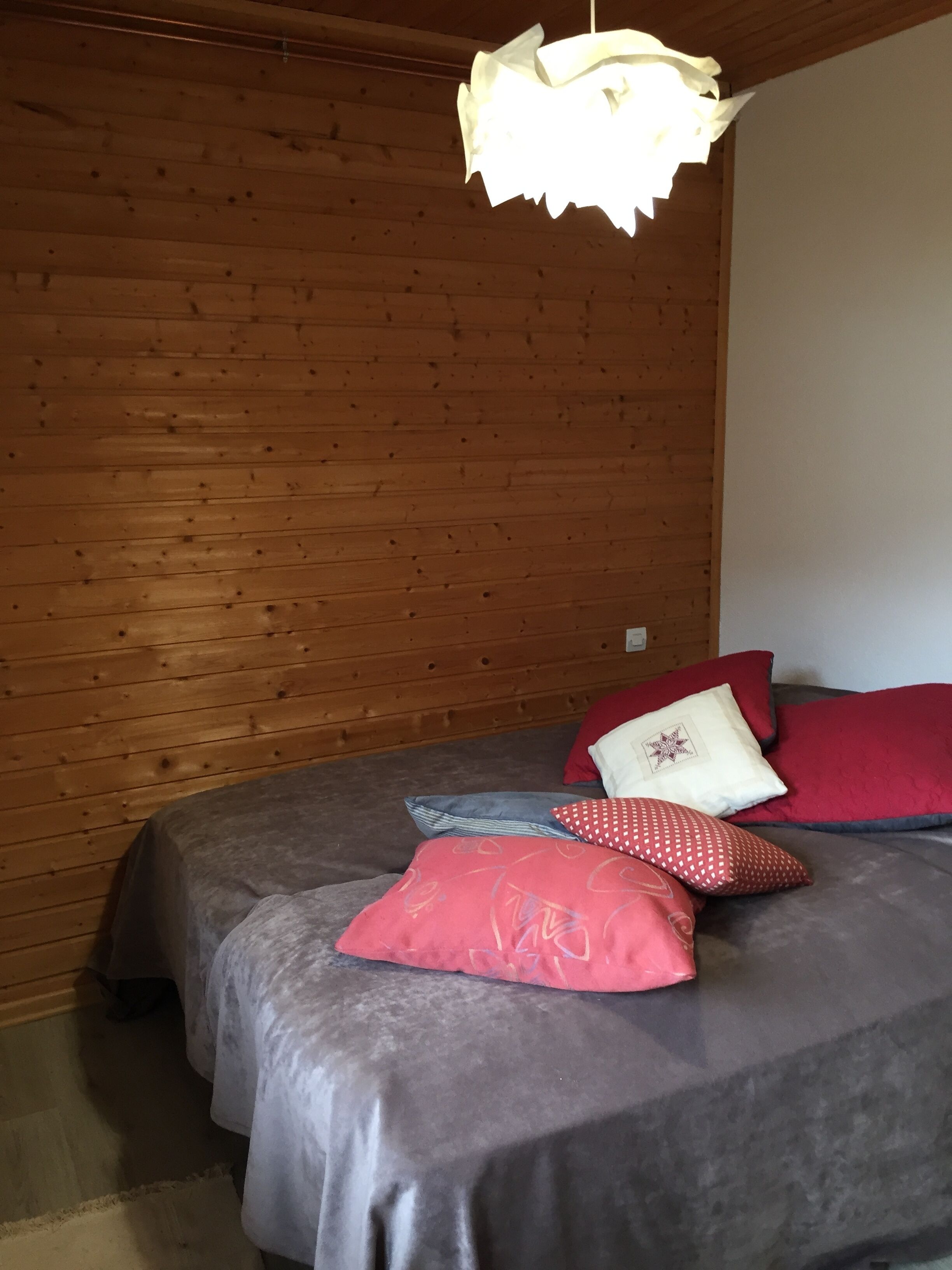 A wooden-paneled room with a bed, pillows, and a hanging light fixture.