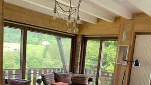 A spacious living room with a large window, a glass coffee table, leather sofas, and a patterned rug. - Chalet "Les Pommes de Pin", sleeps 10-12, 8 rooms, with terrace and garden (La Bresse)