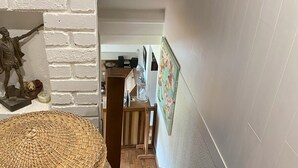 A staircase with a woven basket and a patterned rug, leading to a room with a wooden door and a white brick wall. - Chalet "Les Pommes de Pin", sleeps 10-12, 8 rooms, with terrace and garden (La Bresse)