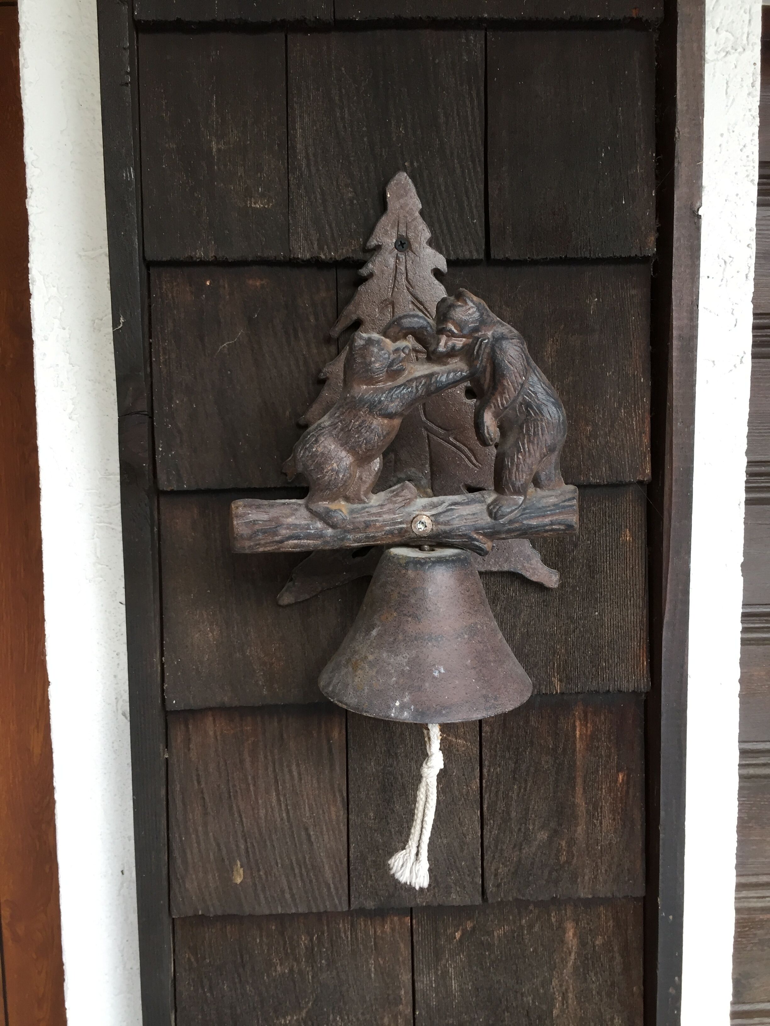 Eine rustikale Holztür mit einem geschnitzten Bild von zwei Bären, die um einen Baumstamm streiten, und einer Glocke.