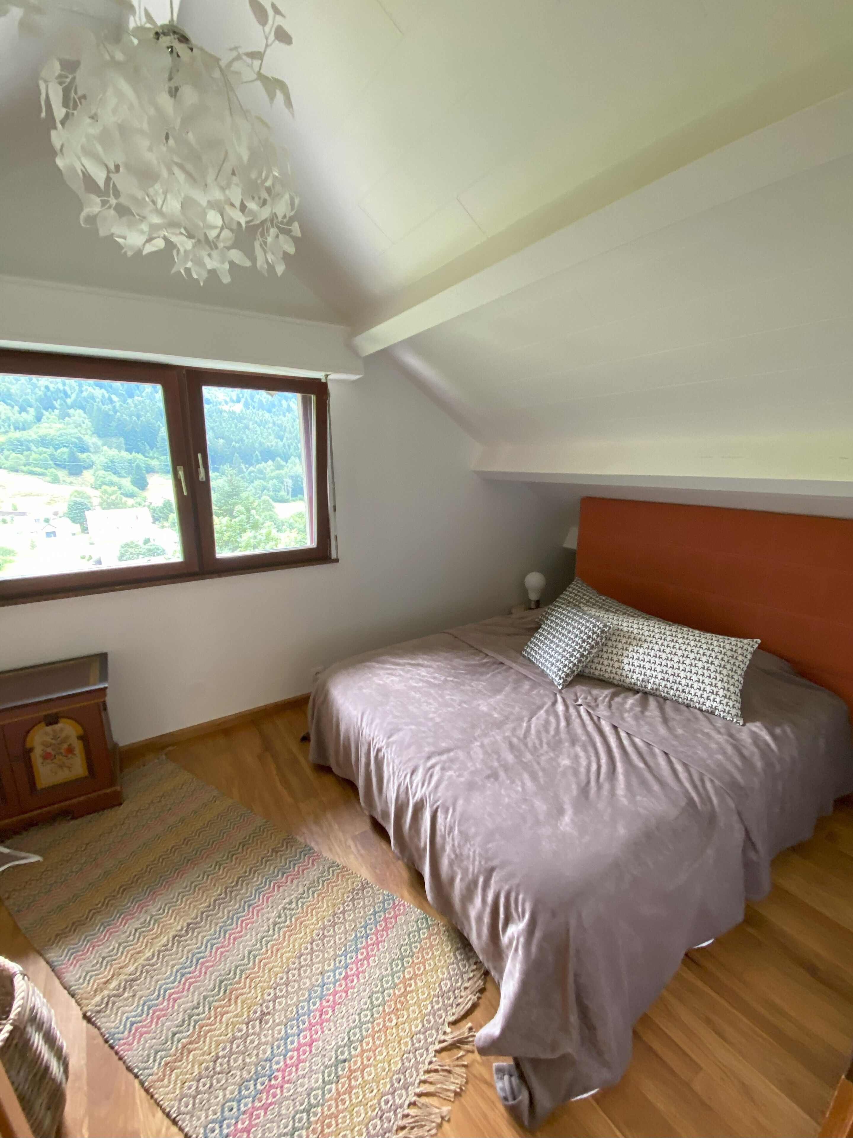 A bedroom with a bed, a window, a ceiling light, and a wooden floor.