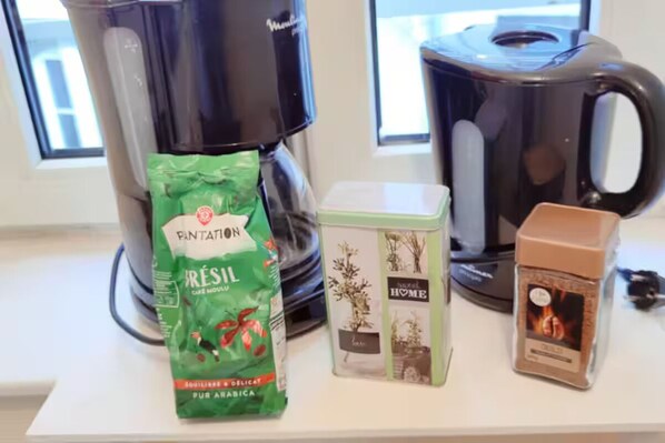 Eine Küchenarbeitsplatte mit einer Kaffeemaschine, einer Packung Ristal-Kaffee, einer Teedose und einer Kaffeeflühse.