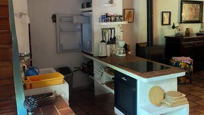 A compact kitchen with a central island, a built-in oven, and a microwave. There are shelves above the island holding various kitchen items. - "Ancien Café " Holiday home (Camplong-d'Aude)