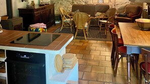 A rustic interior with exposed stone walls, wooden beams, a dining area with chairs and a table, and a kitchen with a stove and a countertop. - "Ancien Café " Holiday home (Camplong-d'Aude)