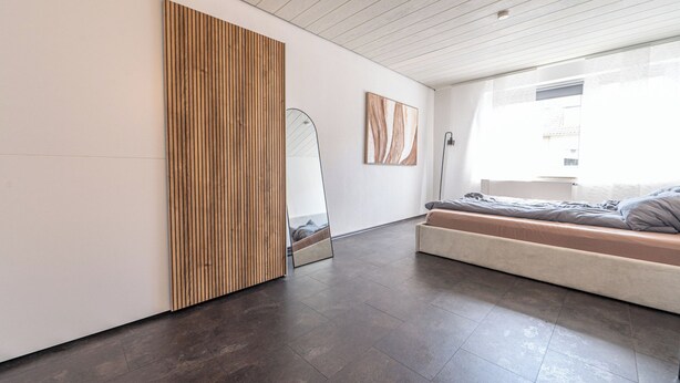 Ein modernes Schlafzimmer mit einem großen Bett, einer Holzwand, einem Spiegel und Kunstwerken.