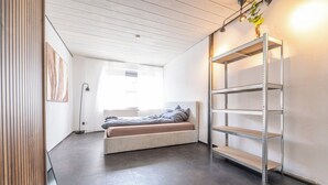 Ein modernes, minimalistisches Zimmer mit integriertem Bett, einer Metallregaleinheit und einem großen Fenster für natürliches Licht.