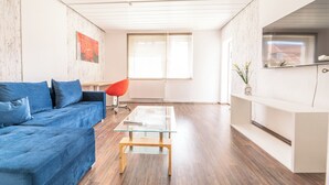 Ein modernes Wohnzimmer mit einem blauen Sofa, einem Glastisch und einem roten Sessel.