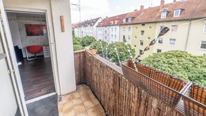 Ein Balkon mit Blick auf terrassenförmig angeordnete Häuser, einen Holzzaun und einen roten Stuhl.