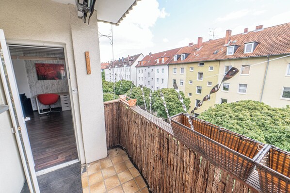 A balcony with a view of terraced houses, a wooden fence, and a red chair. - Modern 2-room apartment near the university - quiet, cozy & close to the city (Braunschweig)