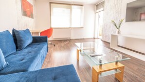 Ein modernes Wohnzimmer mit einem blauen Sofa, einem Glastisch und einem roten Sessel.