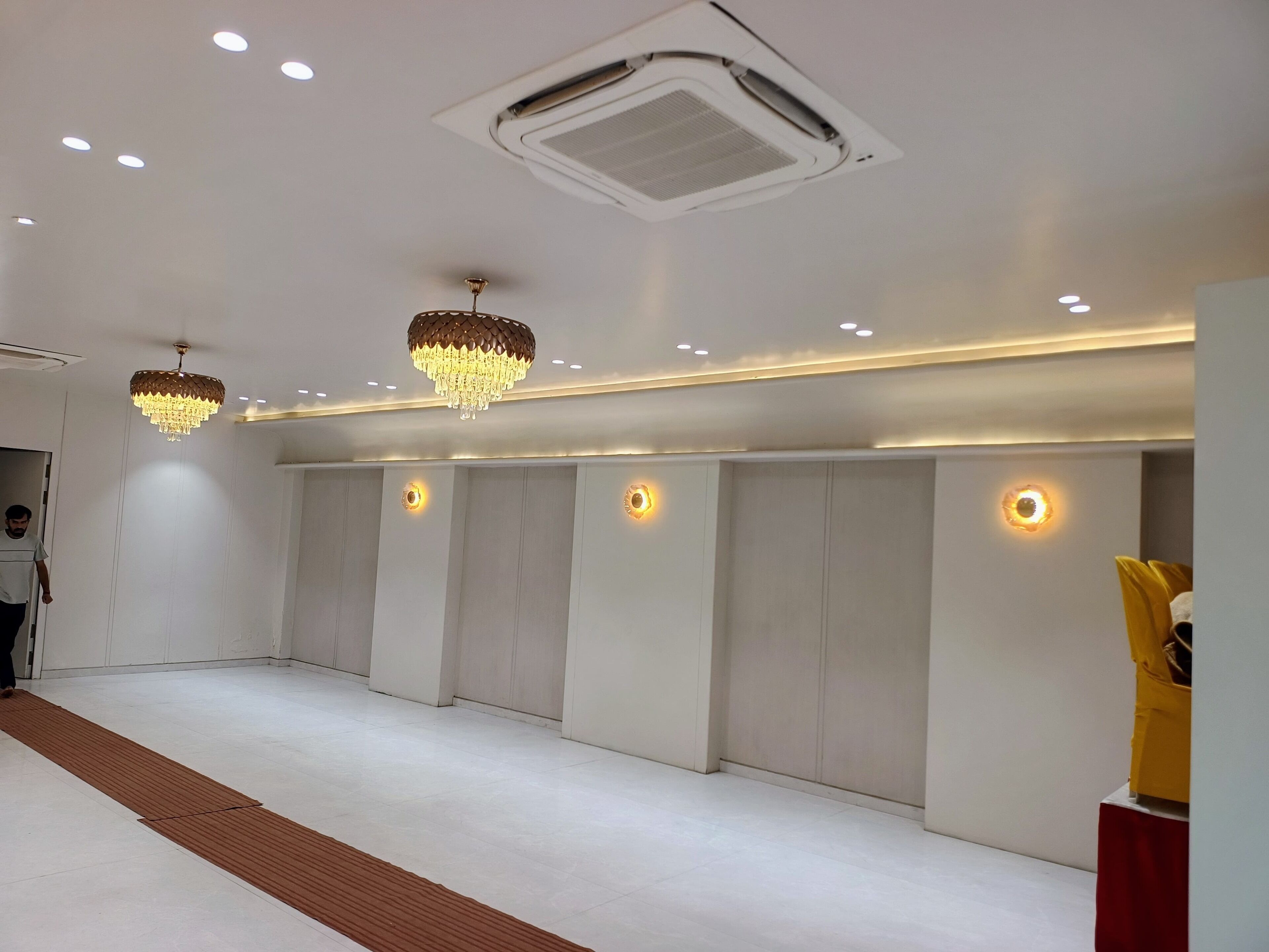 Una habitación amplia con alfombra blanca, iluminación empotrada y un equipo de aire acondicionado grande en el techo.
