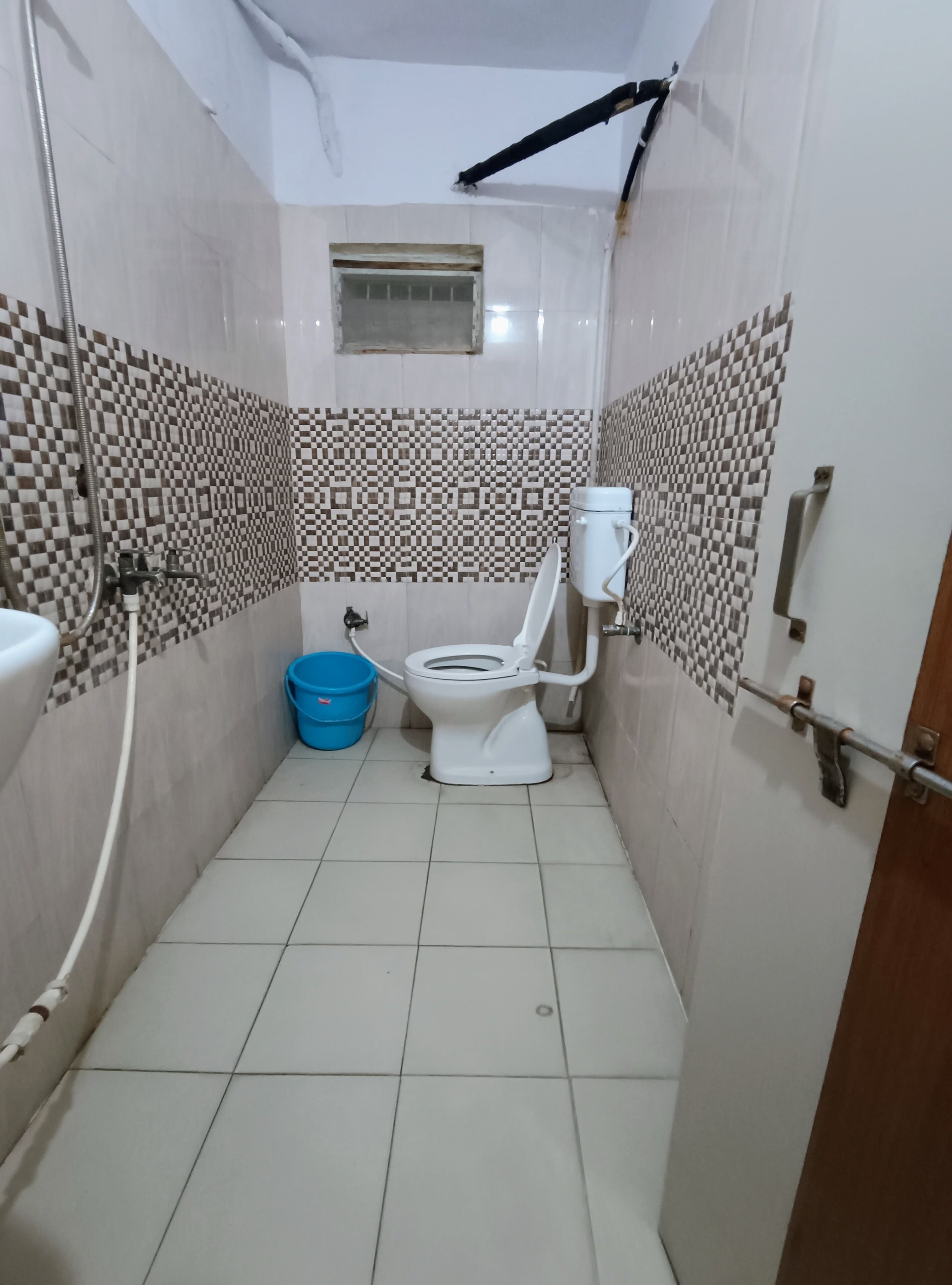 A small bathroom with a toilet, a blue bucket, and tiled walls.