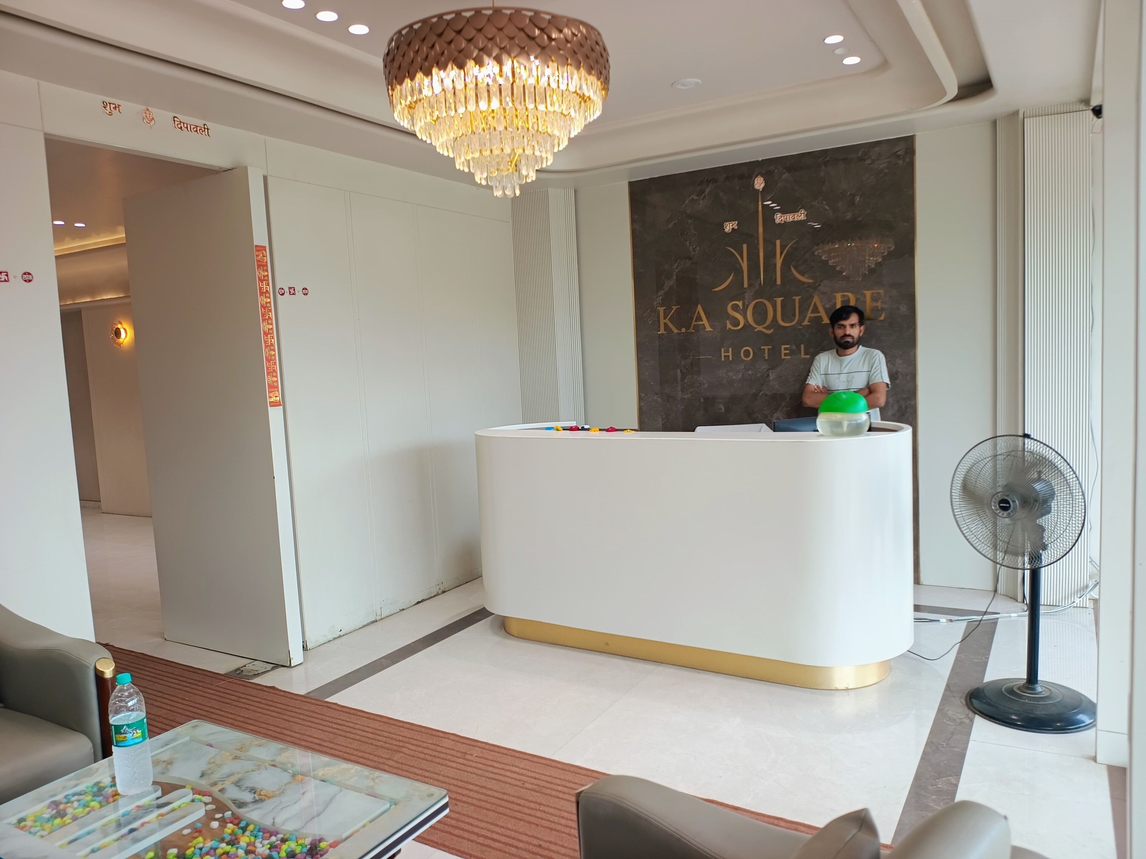 Un hall d'accueil d'hôtel agrémenté d'un lustre moderne, d'un comptoir de réception et d'un mur sur lequel est inscrit le nom de l'hôtel.