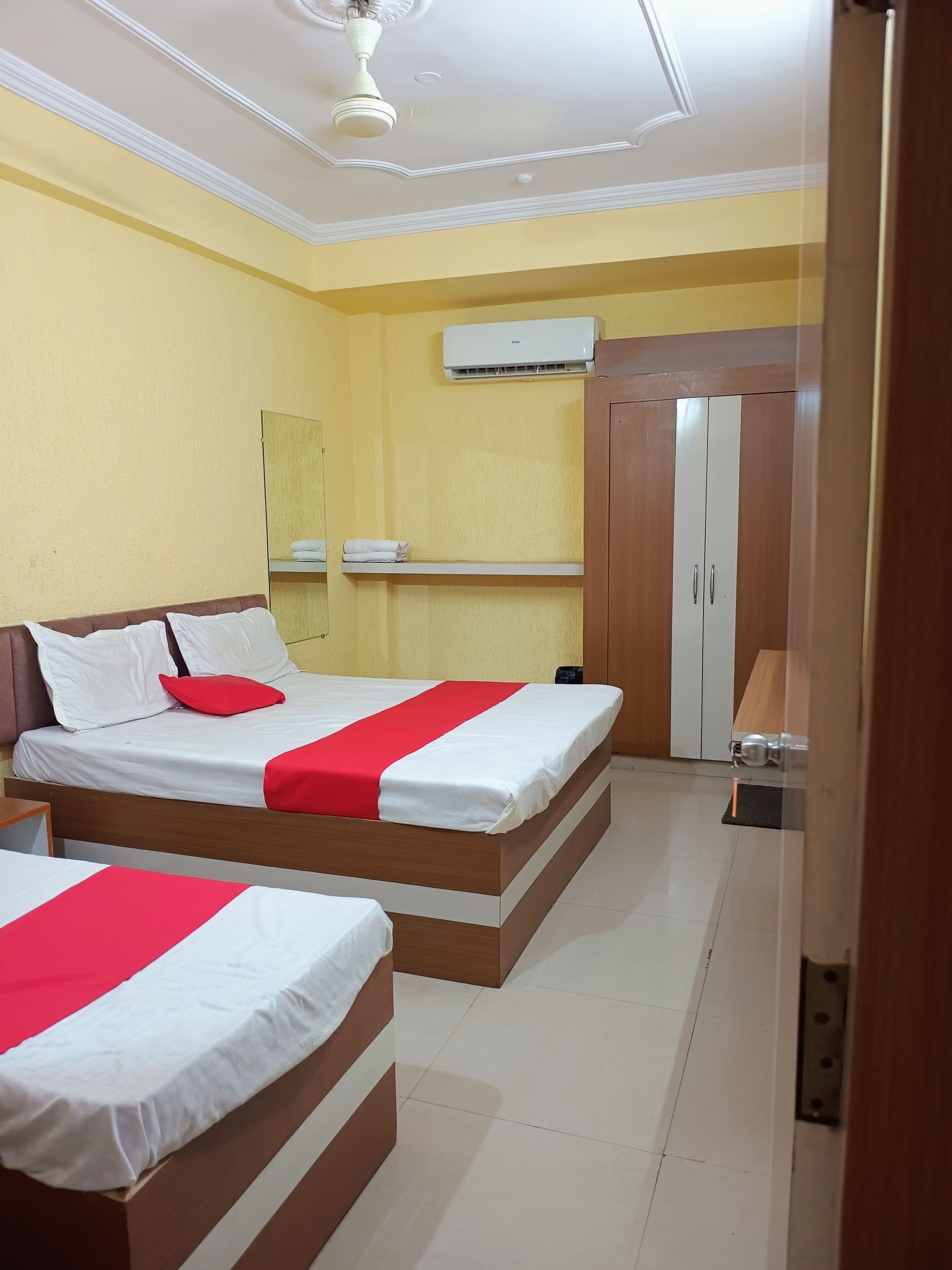 A hotel room with two beds, a wardrobe, an air conditioning unit, and a ceiling fan.