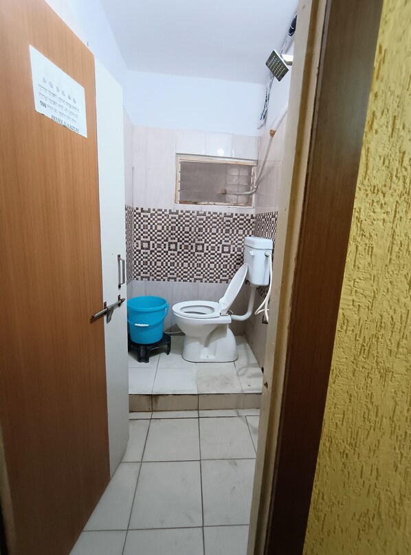 A small, compact bathroom with a toilet, a blue bucket, and a tiled floor.