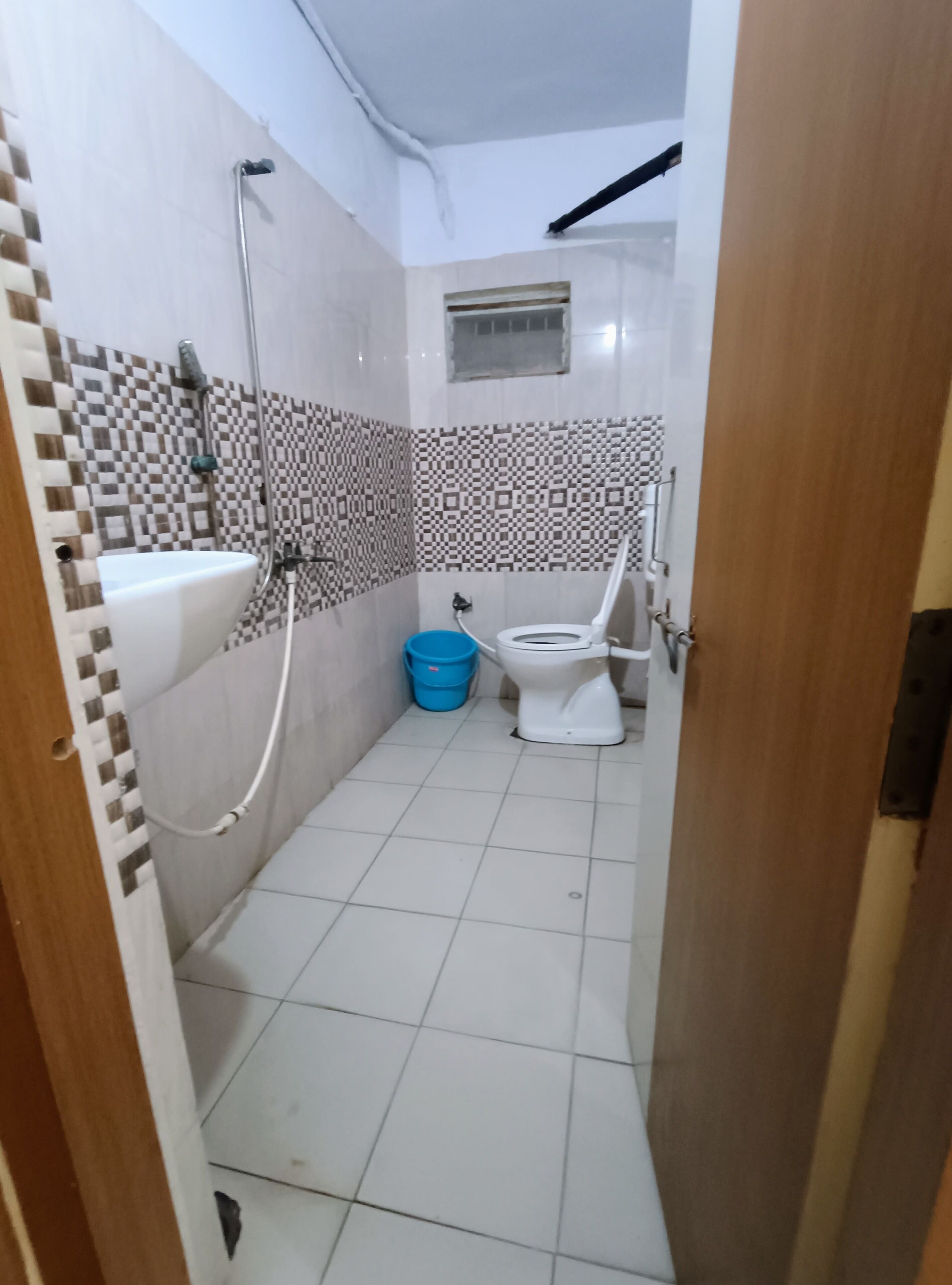Uma casa de banho pequena com sanita, lavatório e chuveiro. Há um balde azul ao lado da sanita.