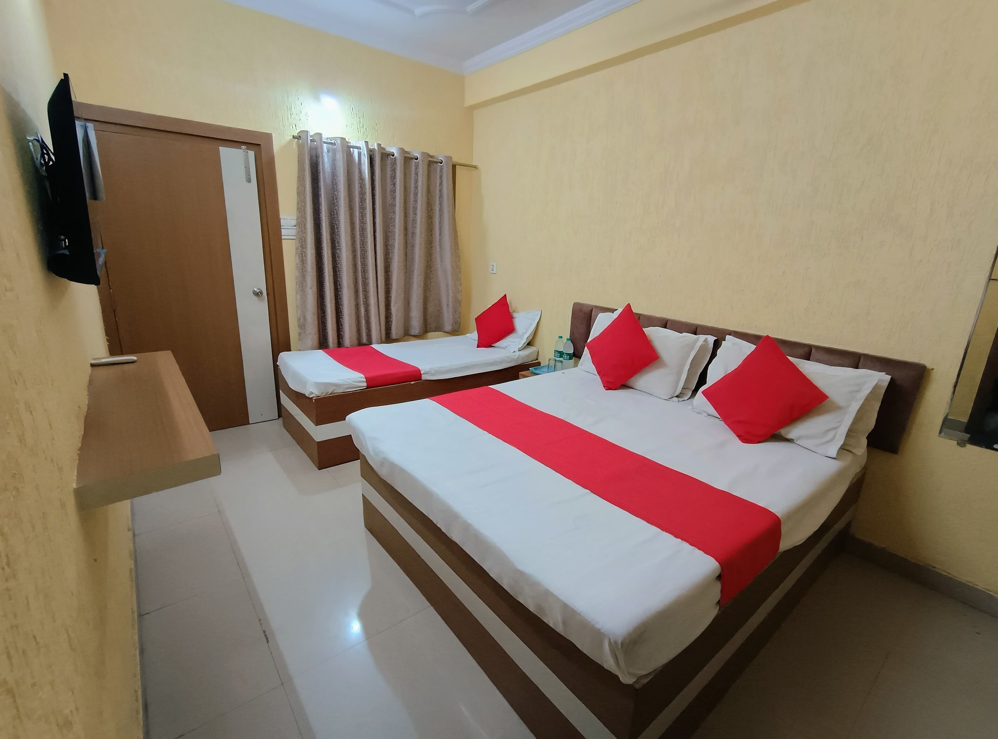 A hotel room with two beds, a television, a curtain, and a bottle of water on the nightstand.