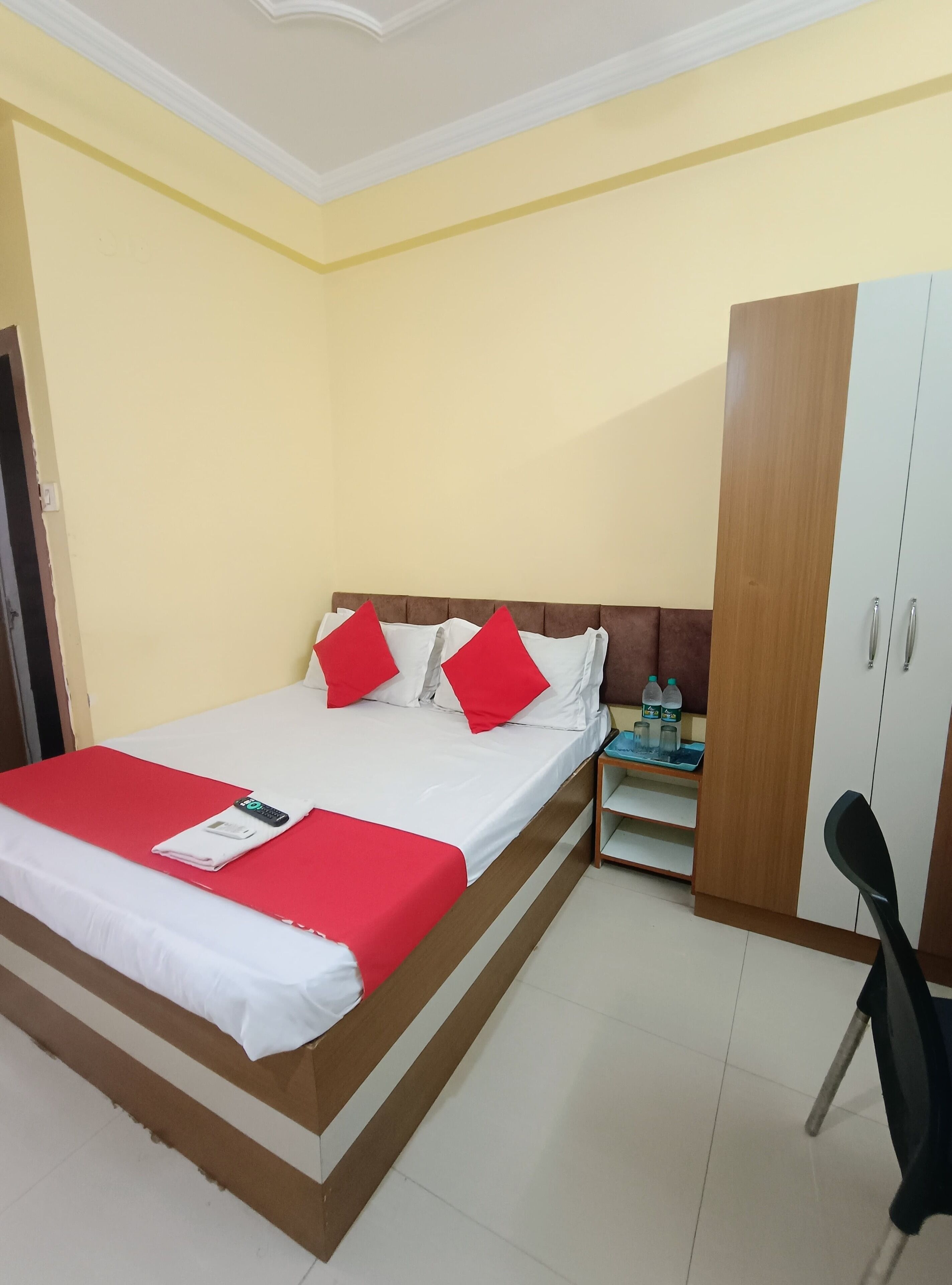 A neatly made bed with red and white bedding, a wooden wardrobe, and a small desk with a chair.