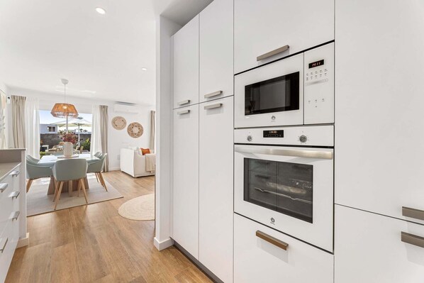 Une cuisine moderne avec des meubles blancs, un four encastré et un four à micro-ondes.