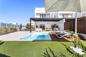 Un área de piscina moderna al aire libre con vistas despejadas al horizonte de la ciudad, una zona de estar cubierta y un césped bien cuidado.