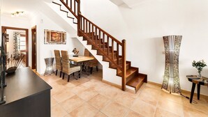 Un salón amplio con una escalera de madera, una mesa de comedor con sillas y un jarrón decorativo sobre una mesita.