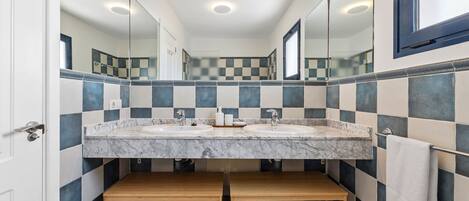A bathroom with a checkered tile backsplash, two sinks with marble countertops, wooden benches, and a large mirror.