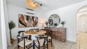 A dining area with a round table, four chairs, a ceiling fan, wall-mounted artwork, a mirror, and a wooden cabinet.