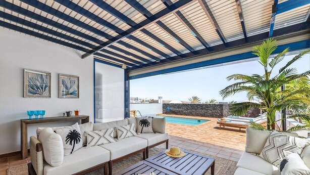 A spacious outdoor seating area with a pool, a wooden coffee table, and a view of the sea.
