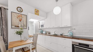 A modern kitchen with white cabinets, a wooden countertop, a sink, a microwave, a kettle, and a dining area with a table and chairs. - Apt. Casa Coco - Aura Villas (Playa Blanca)