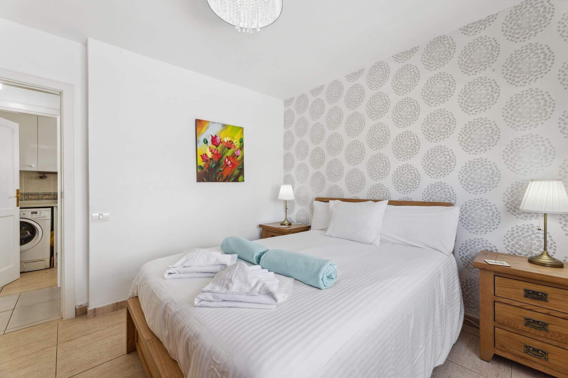 Une chambre d’hôtel avec un lit, une table de chevet, une lampe, un tableau et un lave-linge dans un coin.