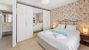 A bedroom with a large bed, a wardrobe, a mirror, and floral wallpaper. - Apt. Casa Coco - Aura Villas (Playa Blanca)