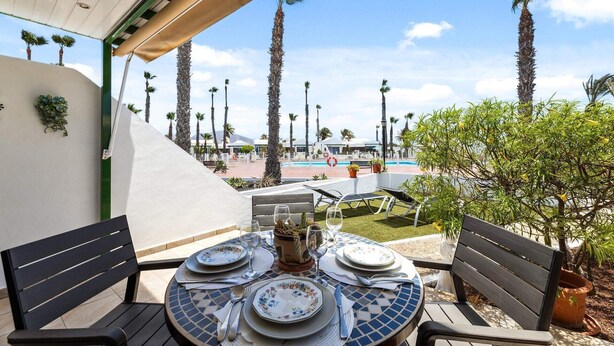 An outdoor dining area with a view of a pool and palm trees. - Apt. Casa Coco - Aura Villas (Playa Blanca)