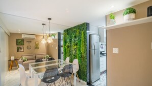 Une cuisine moderne dotée d’un réfrigérateur encastré, un coin repas avec une table et des chaises en verre, et un salon avec un canapé et une table basse.