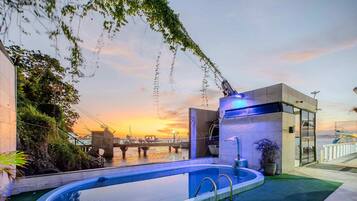 Une piscine avec un pont en arrière-plan, un bâtiment moderne agrémenté d’un élément aquatique et une vue sur le coucher de soleil.