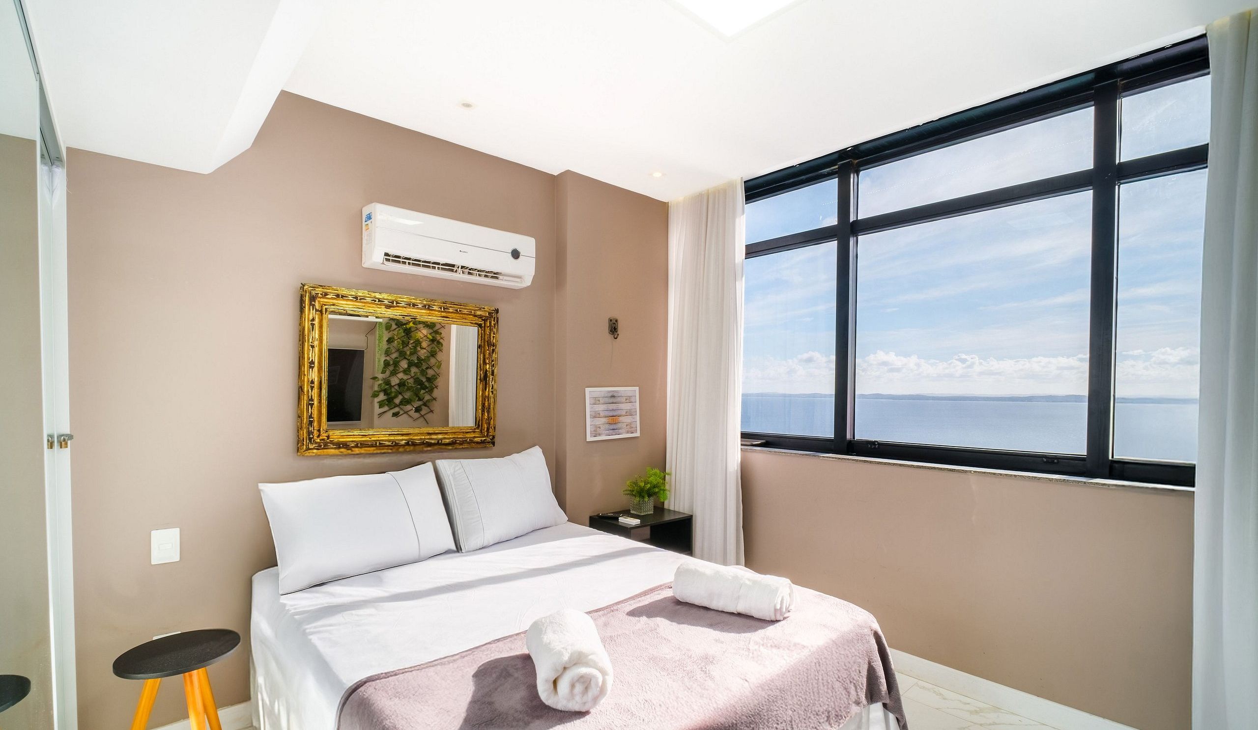 Une chambre d’hôtel avec un lit, une fenêtre donnant sur un paysage agréable, un appareil de climatisation, un miroir et une petite table.