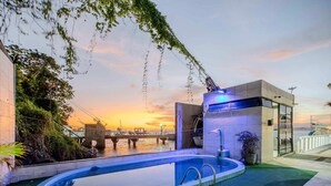 Une piscine avec un pont en arrière-plan, un bâtiment moderne agrémenté d’un élément aquatique et une vue sur le coucher de soleil.