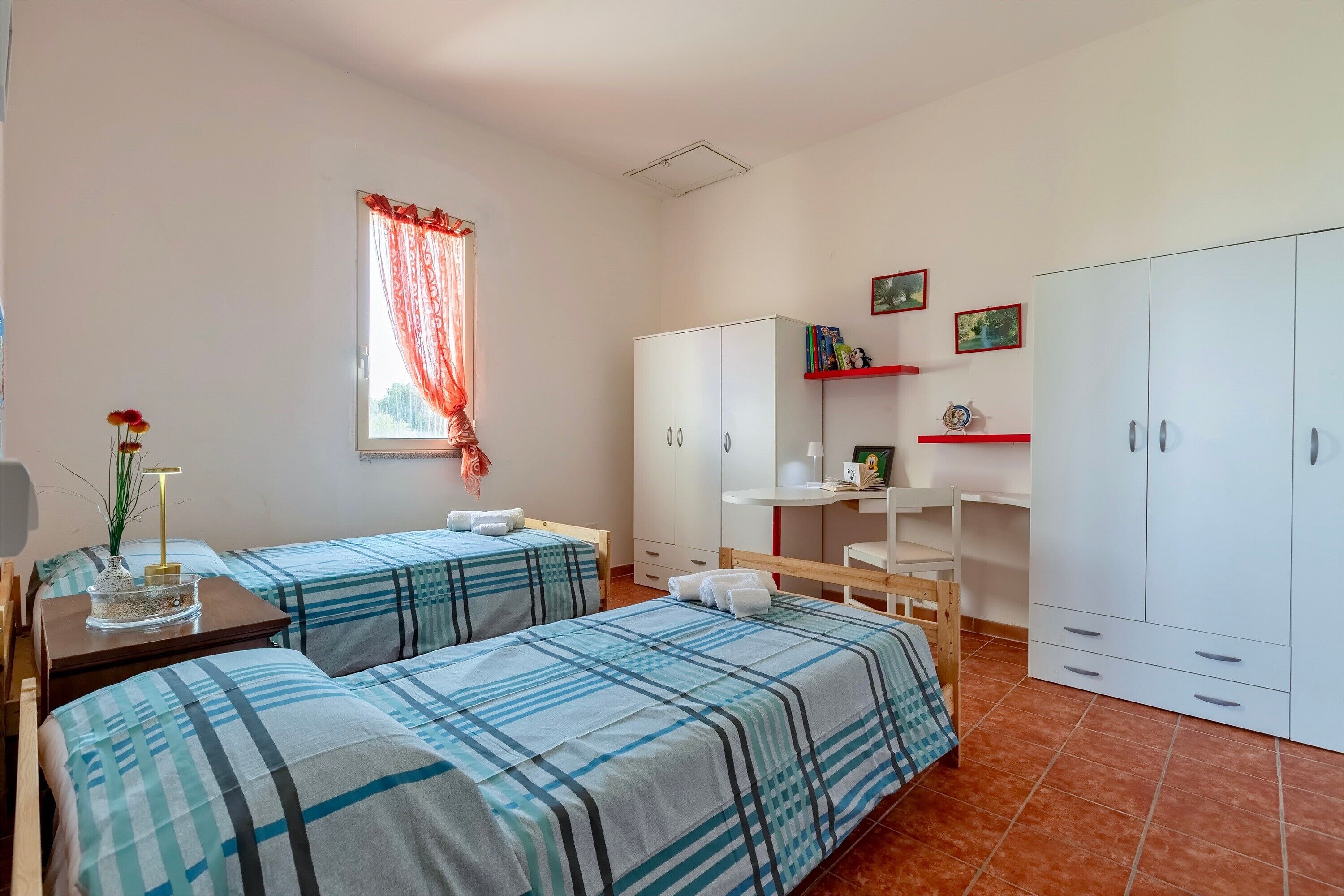 Una habitación con dos camas, un escritorio, un armario y una ventana con cortinas.