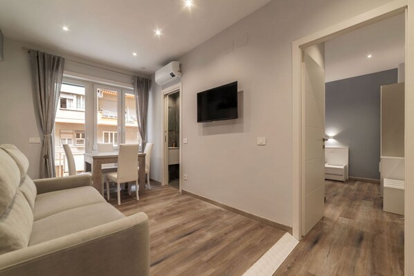 A modern living room with a sofa, a TV mounted on the wall, and a dining area with chairs.