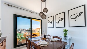 Un coin repas avec une table dressée pour quatre personnes, une vue sur l’extérieur par une porte coulissante et de la calligraphie arabe sur le mur.