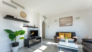 Un salon moderne avec un téléviseur à écran plat, un canapé, une table basse et une grande plante.
