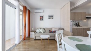 Un salon moderne avec un canapé, une petite table blanche et un coin cuisine à l’arrière-plan.