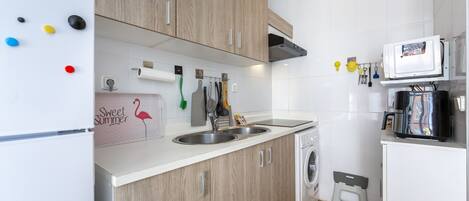 A compact kitchen with wooden cabinets, a built-in washing machine, and a microwave.