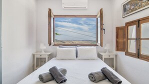 Un dormitorio con una cama grande, dos mesitas de noche con lámparas, una ventana abierta con vistas y un equipo de aire acondicionado.